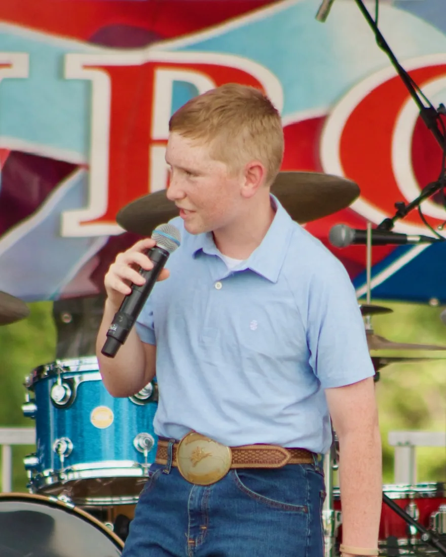 Matthew Watson singing with a microphone on an outdoor stage